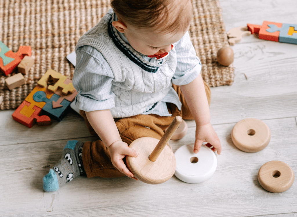 Child playing with wooden stacking toys and puzzle pieces.