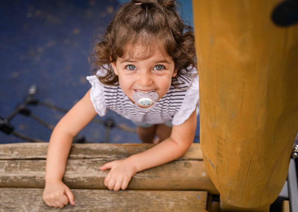 Child with pacifier climbing play structure, looking up.