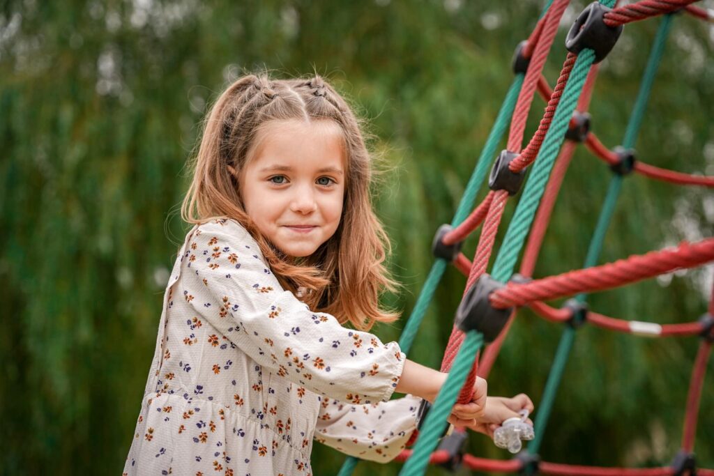Girl playing on red and green rope climbing structure outdoors.